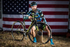 Jake Wells posing with his bicycle in front of an american flag